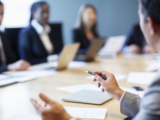 Hands of businessman gesturing ideas decisions with pen pointing leadership to work colleagues in business meeting at board room conference table
