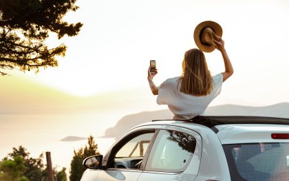 Young woman enjoying a road trip along the coast and taking photo with smart phone