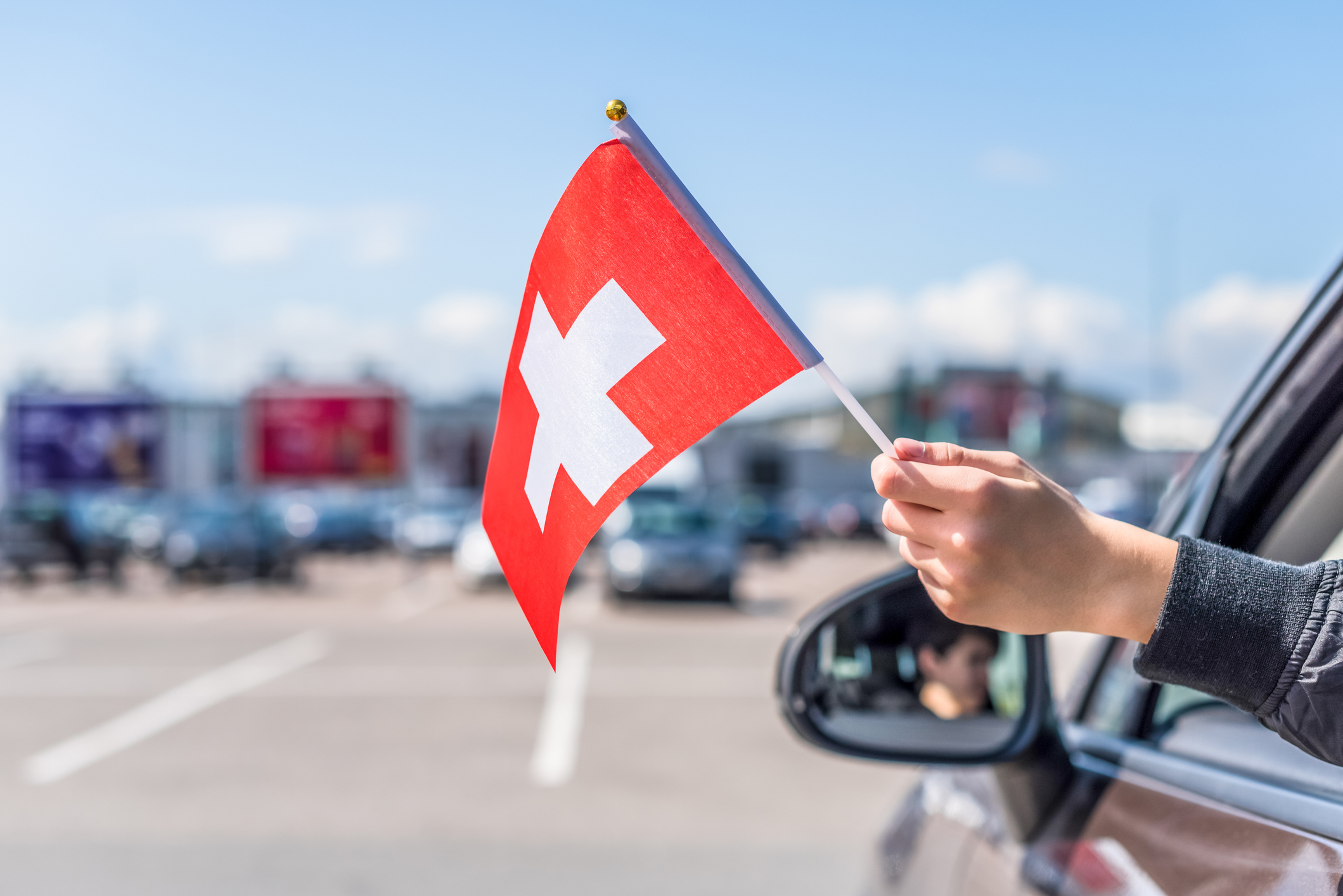 Boy holding Swiss Flag from the open car window on the parking of the shopping mall. Concept. Switzerland